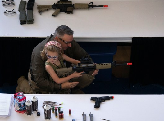 A man shows a girl how to hold an airsoft gun during the NRA Youth Day at the National Rifle Association's annual meeting in Houston, Texas